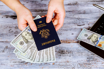 Cropped hands of woman holding passport and paper currency over table