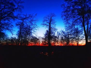 Silhouette trees on landscape against sky at sunset