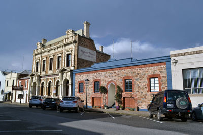 Cars on city street by buildings against sky