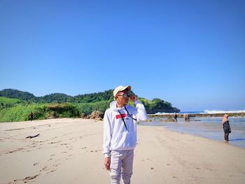 Rear view of woman standing at beach against clear blue sky