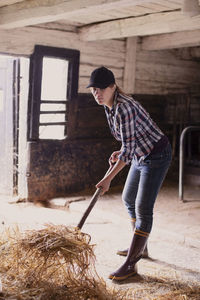 Full length of female farmer shoveling hay in barn