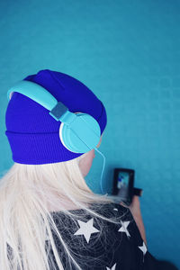 Close-up of woman with blond hair listening music while using mobile phone against blue wall