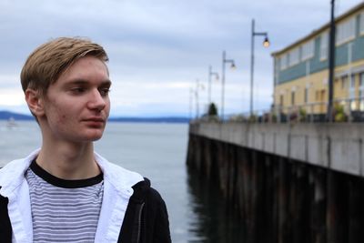 Young man looking away while standing against lake