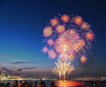 Firework display over illuminated city against sky at night