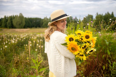 A cute girl in a hat with a brim holds a bouquet of sunflowers in a field