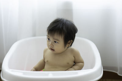 Shirtless baby girl sitting in bathtub