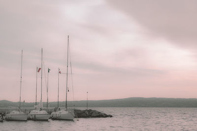 Sailboats moored in sea against sky during sunset