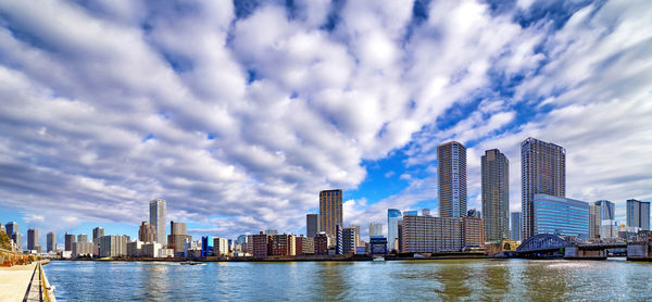 Modern buildings by river against sky in city