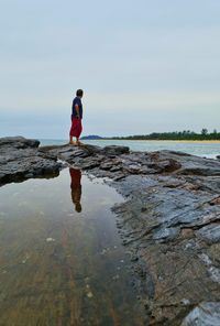 Man standing on rock at beach against sky