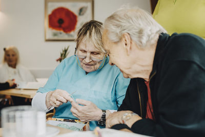 Senior female nurse teaching knitting to elderly man at retirement home