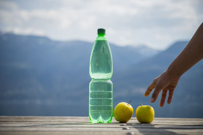 Close-up of hand reaching towards apples and drink bottle on table