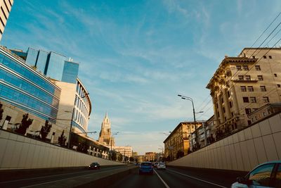 Vehicles on road by buildings against sky