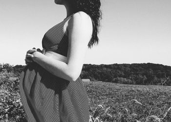 Pregnant woman touching her belly while standing on field against clear sky