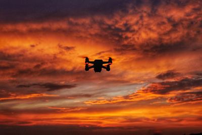 Low angle view of silhouette bird flying against orange sky