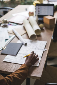 Cropped hand of female designer working over blueprint at home office desk