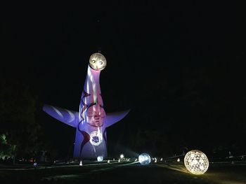 Man standing by illuminated ferris wheel against sky at night