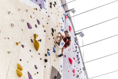 Athlete wearing safety harness and climbing on boulder wall in gym