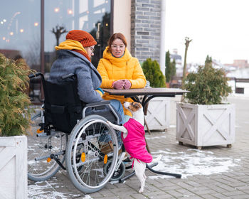Two girlfriends in a cafe on a street terrace in winter. woman in a wheelchair