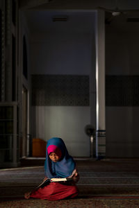 Girl in hijab reading book while sitting at mosque