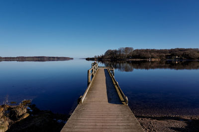 Pier over lake against clear blue sky