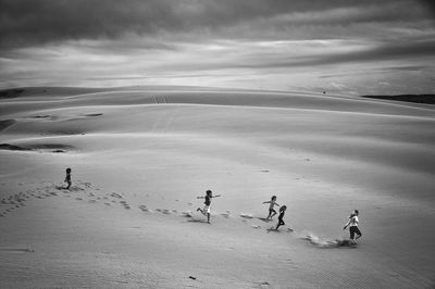High angle view of people running in desert against cloudy sky