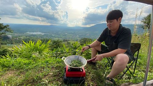 Young man sitting on plants by mountains