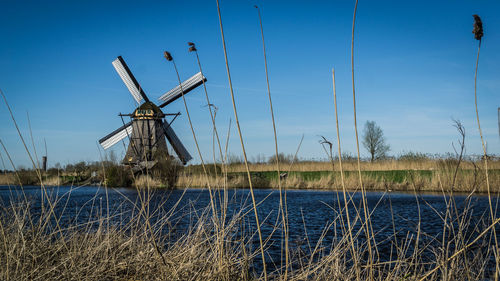 Traditional windmill on field by lake against blue sky