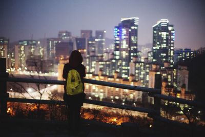 Rear view of woman standing by railing against city