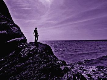 Silhouette woman standing on rock by sea against sky