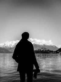 Rear view of silhouette man standing on pier over lake against sky