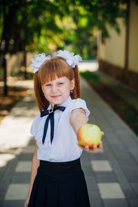 Back to school. a little schoolgirl stands in the school yard and holds an apple in her hands.