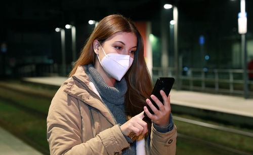 Young woman wearing mask while using mobile outdoors