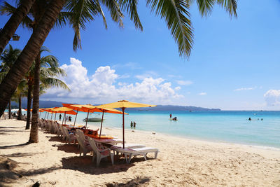 Chairs by parasols in row at sandy beach against blue sky