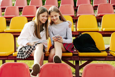 Two schoolgirls watch videos together on a smartphone in the school stands. 