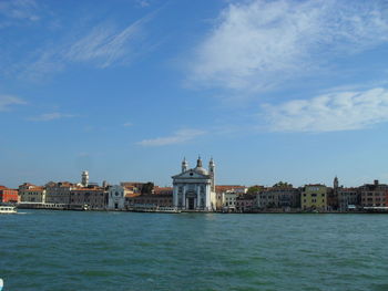 Buildings at waterfront against cloudy sky