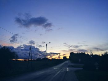 Road by silhouette trees against sky at sunset