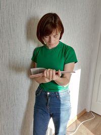 Boy using digital tablet while standing against wall