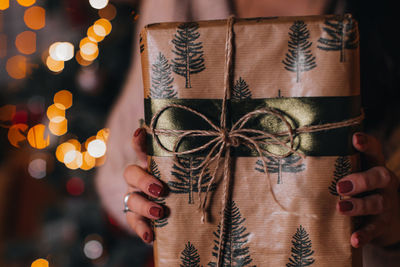 Female hands holding brown christmas gift wrapped in festive paper festive winter holidays concept