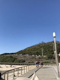 People walking on road against clear blue sky