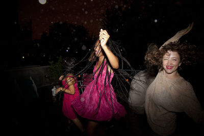 Beautiful young woman standing by palm tree at night