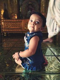 Side view of cute baby girl looking away while sitting on floor in temple