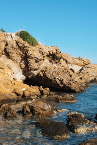 Rock formations by sea against clear blue sky