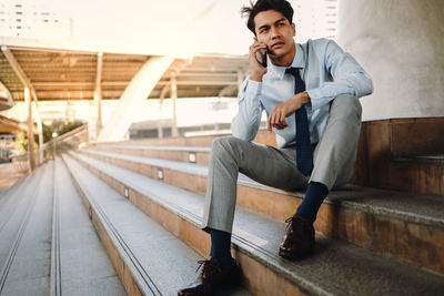 Full length of young man looking away while sitting on mobile phone