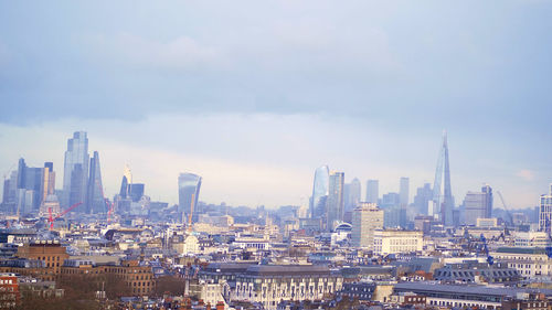 Aerial view of buildings in city against cloudy sky