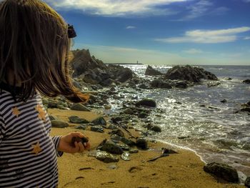 Rear view of woman standing on beach against sky