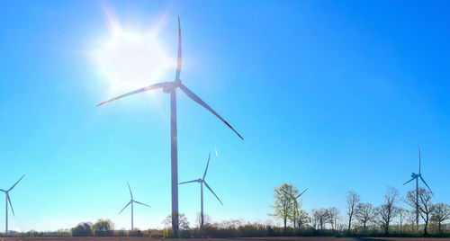 Low angle view of wind turbines on field against sky