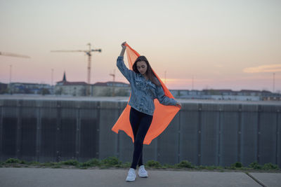 Woman with orange textile standing against sky during sunset