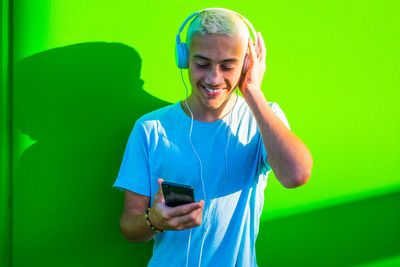 Smiling boy listening music while standing against green wall