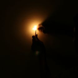 Silhouette person holding lit candle against black background