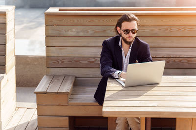 Businessman using laptop while sitting on bench outdoors